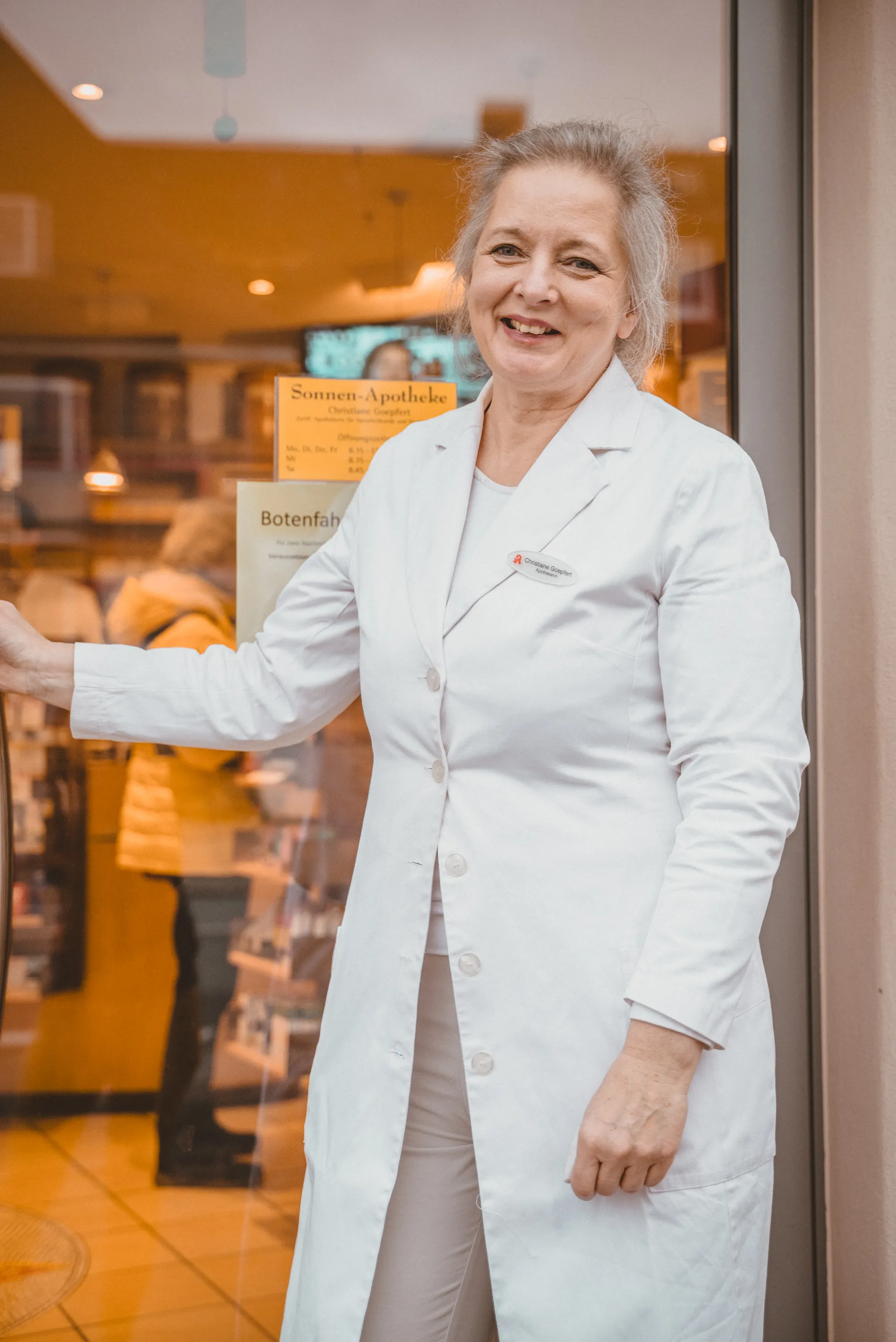 Inhaberin Christiane Goepfert lächelt frontal an Eingangstür der Sonnen-Apotheke